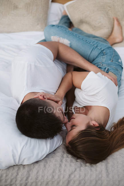Casal romântico em camisetas brancas e jeans deitado e abraçando no quarto de glamping — Fotografia de Stock