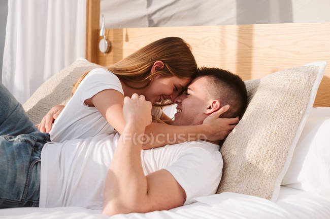 Passionate couple in white t-shirts and jeans lying and hugging in bedroom of glamping — Stock Photo