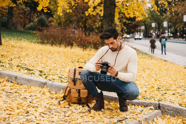 Schöner junger Fotograf im Herbstpark, der sich Fotos vor der Kamera ansieht — Stockfoto