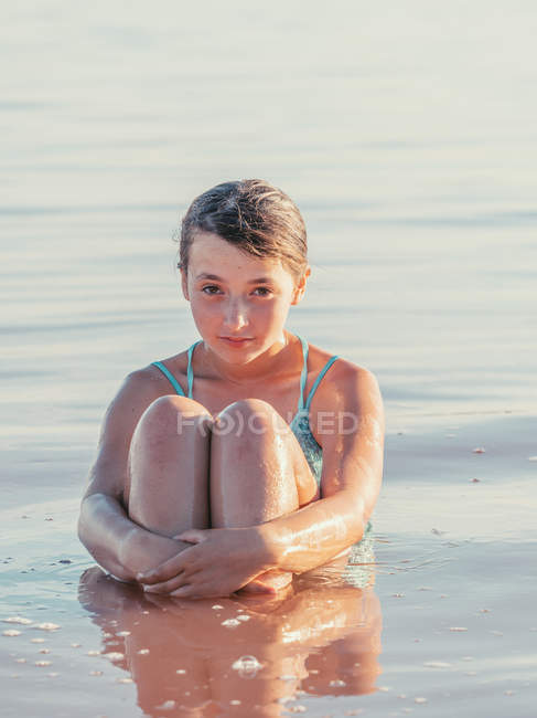 Nachdenkliches Mädchen, das im Wasser sitzt und an heißen Tagen in die Kamera schaut — Stockfoto