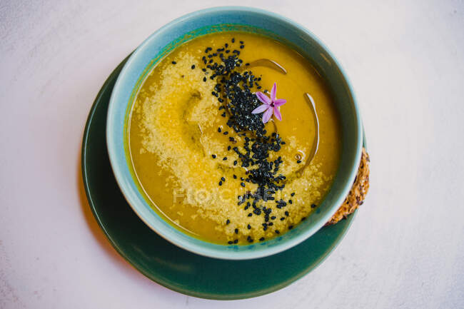 Зверху жовтий суп пюре з чорним насінням у синій мисці та вівсяним хлібом на тарілці — стокове фото