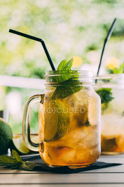 Cocktail di mojito preparato con lime, menta, rum, soda e ghiaccio in vasetto di muratore in tavola all'aperto — Foto stock