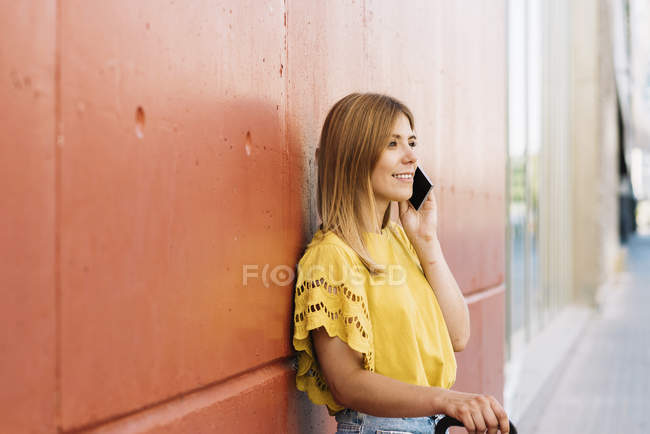 Jovem mulher falando no celular inclinado na parede vermelha — Fotografia de Stock