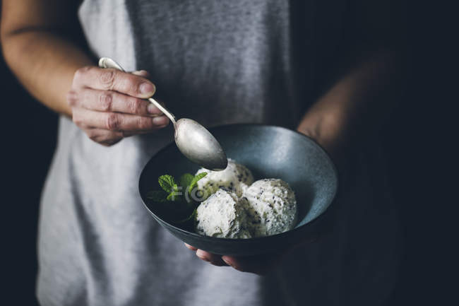 Female hands with spoon holding bowl with stracciatella ice cream balls decorated with mint leaves — Stock Photo