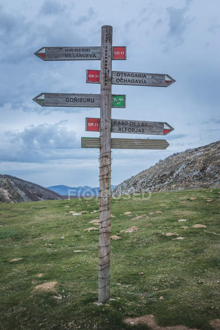 Shabby wooden post with direction signs located on grassy hillside against cloudy sky in nature — Stock Photo
