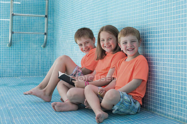 Kinder sitzen im leeren Pool und lesen Buch — Stockfoto