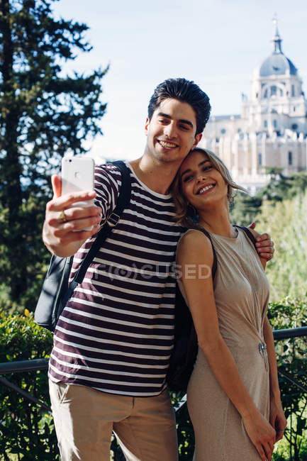 Joven hombre guapo tomando selfie con novia mientras camina en hermoso jardín - foto de stock