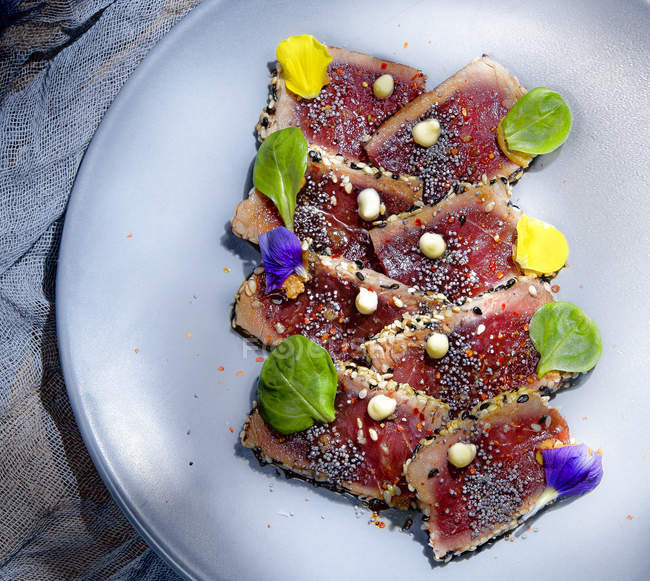 Dall'alto deliziosi pezzi di tataki di tonno fresco appetitosi con foglie verdi sul piatto — Foto stock
