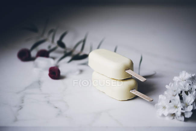 Eis am Stiel aus weißer Schokolade gestapelt auf einer mit Blumen verzierten Marmoroberfläche — Stockfoto