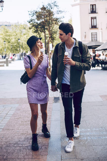 Jovem alegre atraente mulher e namorado andando de mãos dadas enquanto come sorvete ao ar livre — Fotografia de Stock