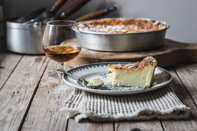 Cottage cheese baked pudding served on plate on towel and glass of cognac on wooden table — Stock Photo