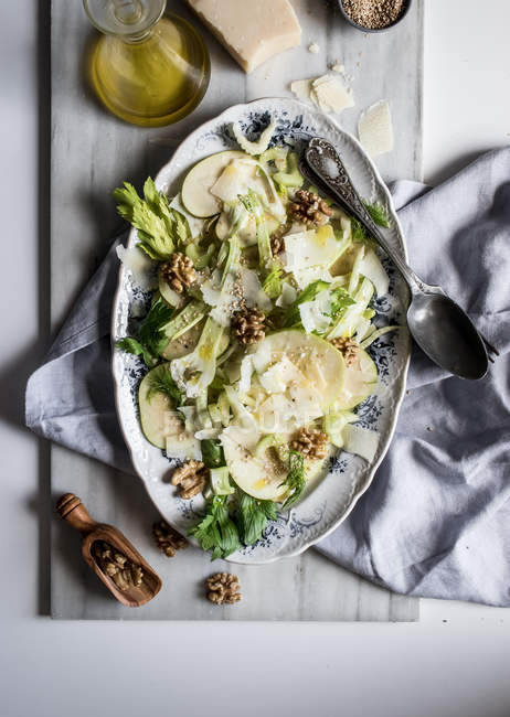 Von oben mit köstlichem Salat aus Äpfeln, Parmesan, Walnüssen, Sellerie und Öl auf dem Tisch — Stockfoto