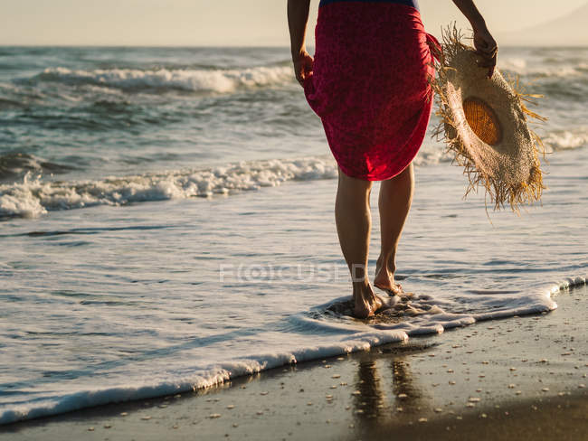 Visão traseira pernas cortadas femininas andando ao longo da costa em luz solar brilhante — Fotografia de Stock