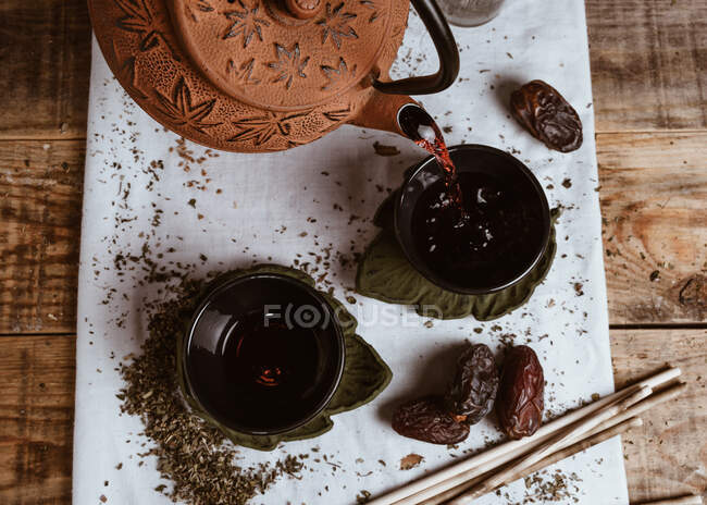 Servindo chá saboroso fragrante em xícara bule de barro e datas doces na bandeja branca decorada com folhas de chá no fundo de madeira — Fotografia de Stock