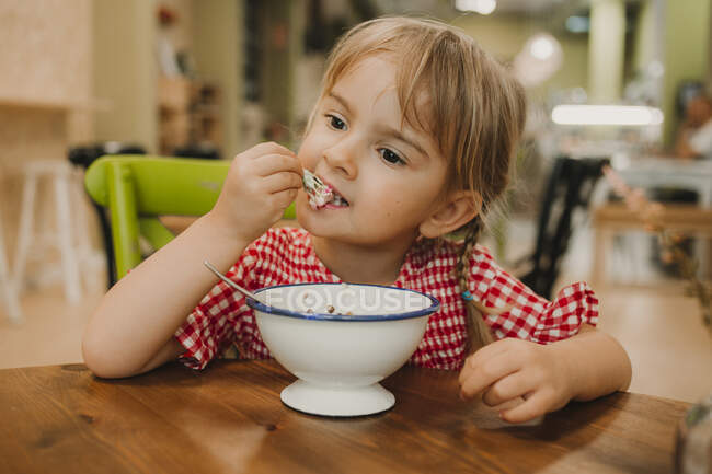 Appetitlich duftendes Essen in weißer Schüssel und entzückendes Mädchen, das mit den Händen am Tisch isst — Stockfoto