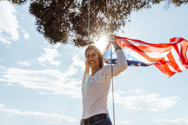 Chica joven celebrando el 4 de julio con la bandera americana en un columpio - foto de stock