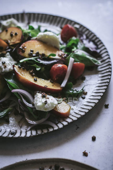 Plate with gourmet salad made of peaches, red onion, cheese and black pepper on table — Stock Photo
