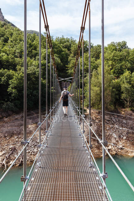 Back view of unrecognizable man with backpack doing trekking while crossing a metal wire bridge — Stock Photo