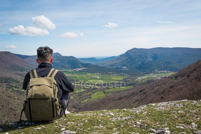Вид ззаду чоловічий мандрівник, що сидить на горі, захоплюючий мальовничий вид на горбисту долину — стокове фото