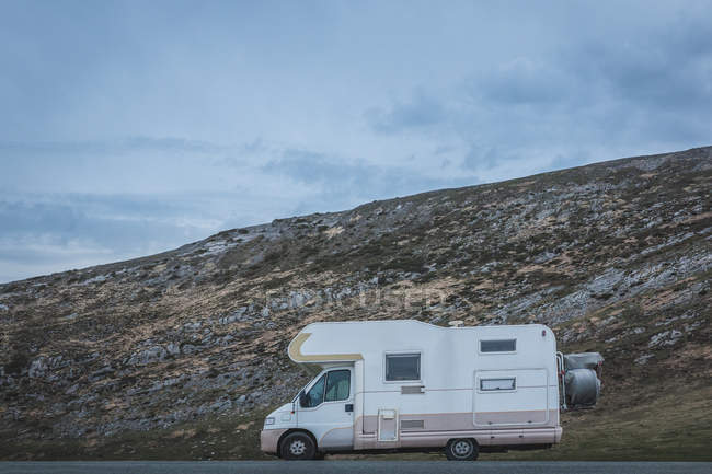 Trailer blanco estacionado cerca de la cuesta de la colina áspera en el día gris cubierto en el campo. - foto de stock