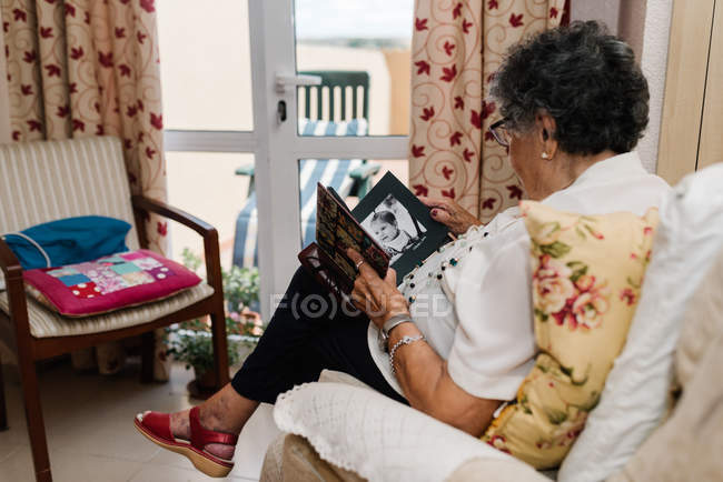 Donna anziana in occhiali guardando la foto della nipote in album a casa — Foto stock
