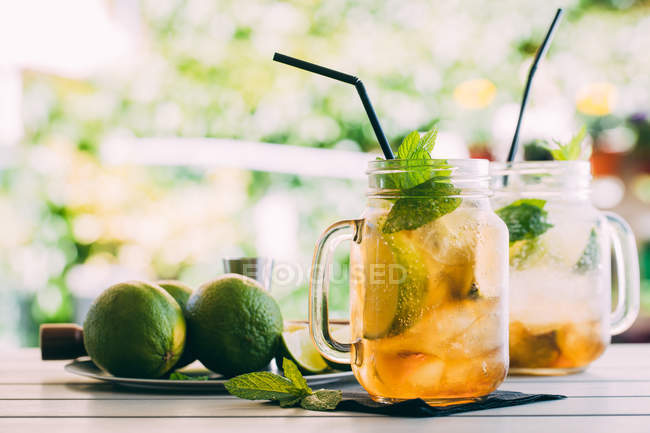 Two mojito cocktails prepared with lime, mint, rum, soda and ice in mason jars on table outdoors — Stock Photo
