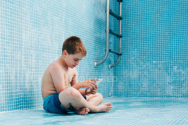 Garçon avec smartphone assis sur le fond de la piscine vide — Photo de stock