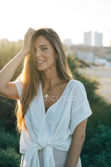 Молодая привлекательная женщина в белой одежде улыбается и смотрит в камеру на улице — стоковое фото