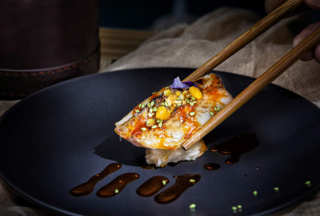 Appetizing delicioso sushi colorido com molho vermelho e sementes verdes tomadas com pauzinhos na mesa servida no restaurante — Fotografia de Stock