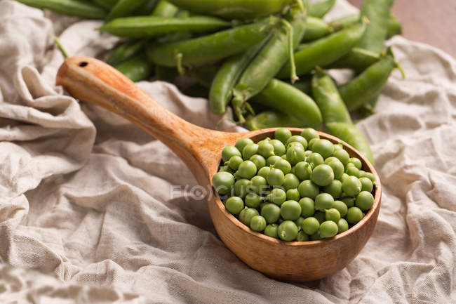 Fresh peas in wooden scoop on rustic cloth — Stock Photo