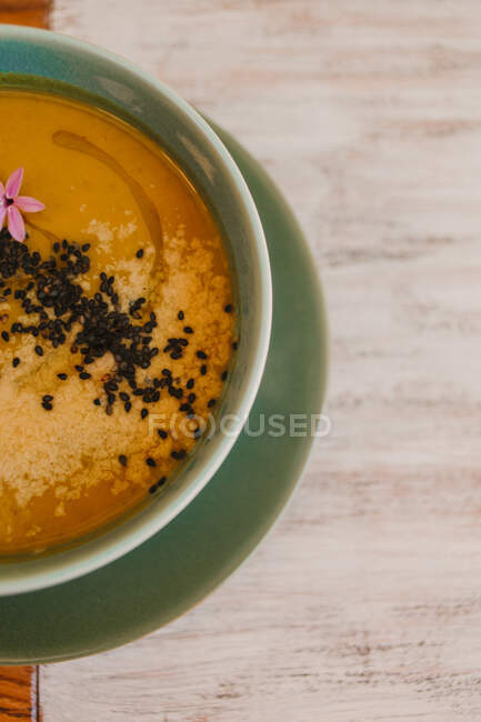 З верхнього жовтого супового пюре з чорними насінинами в блакитній чаші. — стокове фото