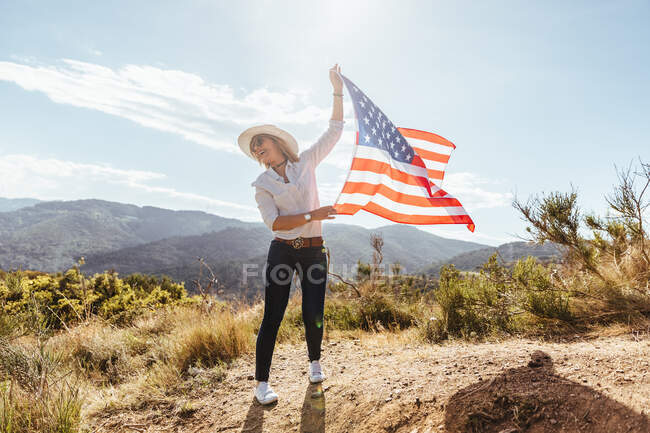 Chica joven celebrando el 4 de julio con una bandera americana al atardecer - foto de stock