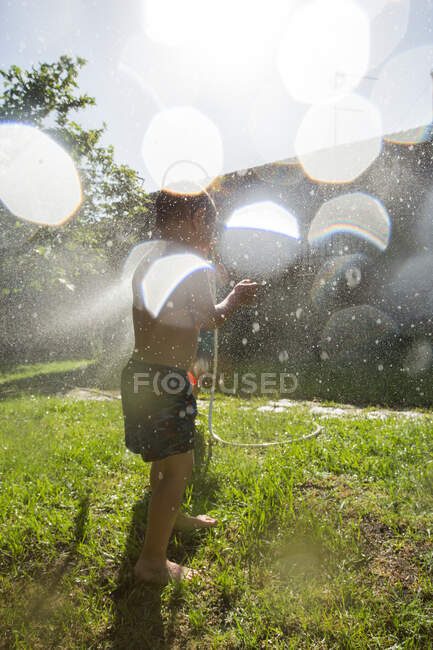 Niños pequeños anónimos en traje de baño corriendo y salpicando el agua de la manguera del jardín entre sí - foto de stock