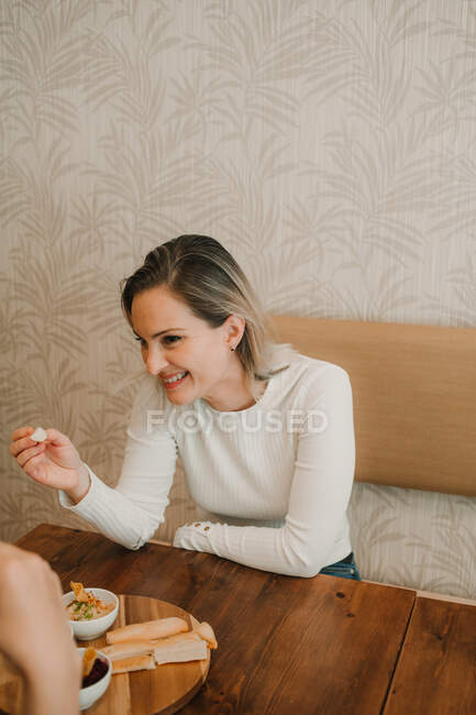 Attractive young woman having lunch with friend and tasting appetizing snack at table — Stock Photo