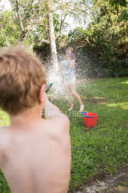 Маленькі діти в купальнику бігають навколо і розбризкують воду з садового шланга один на одного — стокове фото