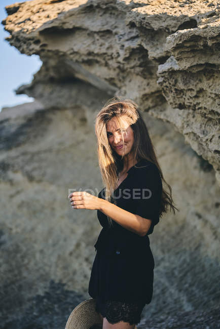 Jovem de cabelos longos sorridente mulher olhando para a câmera contra a rocha — Fotografia de Stock