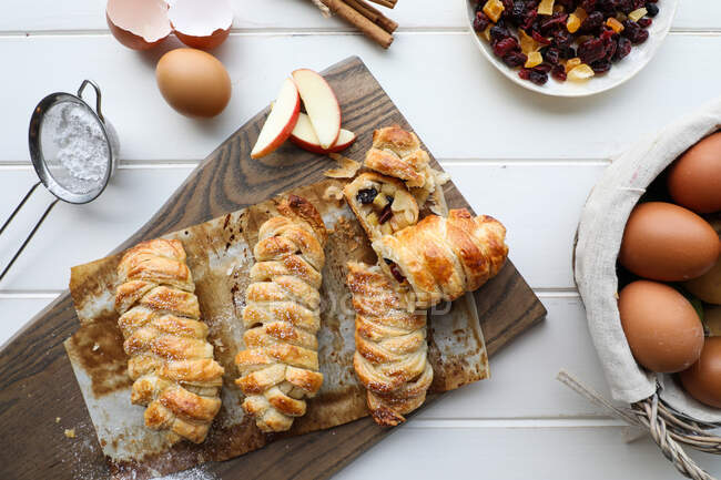 Von oben köstliche frische Strudel mit süßen Äpfeln und Rosinen auf einer weißen Tischplatte neben Sieb und rohen Eiern — Stockfoto