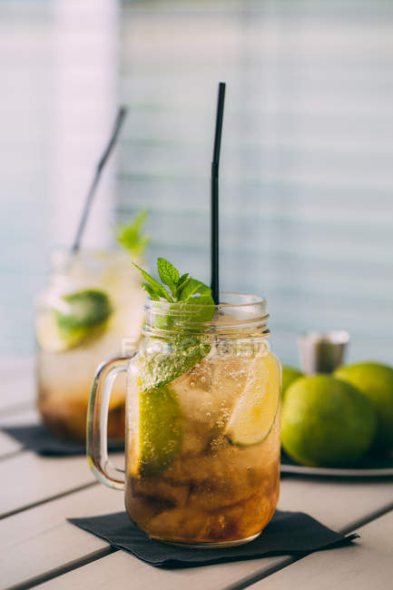 Two mojito cocktails prepared with lime, mint, rum, soda and ice in mason jars on table — Stock Photo