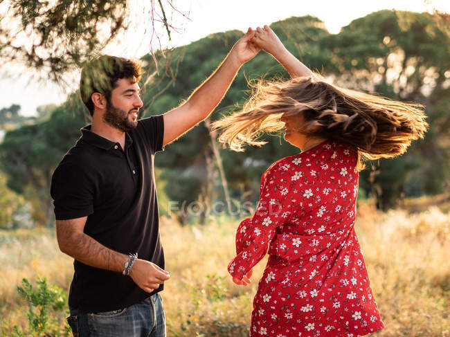 Чоловік і весела вагітна дружина танцює на фоні мальовничого зеленого парку в сонячний день — стокове фото