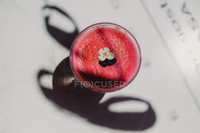 Smoothie rose parfumé mousseux mousseux décoré de fleurs en verre sur une surface blanche avec ombre — Photo de stock