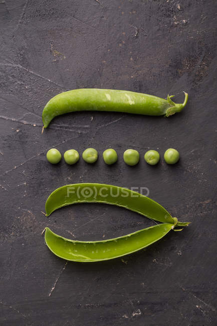 Peeled fresh peas and pea pods on dark background — Stock Photo