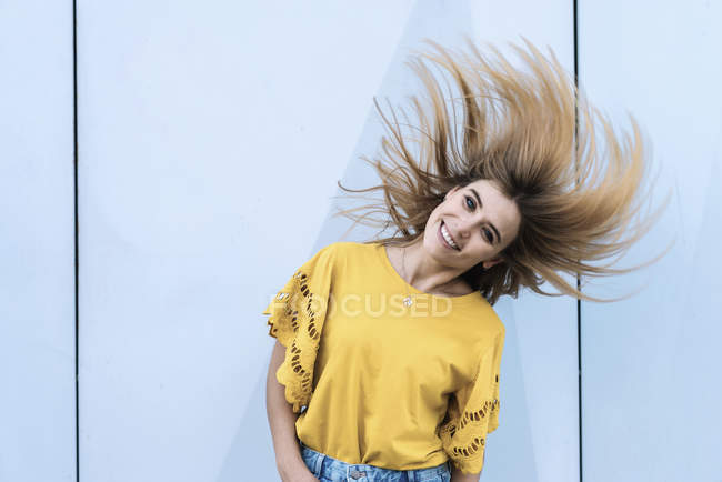Jeune femme joyeuse secouant les cheveux et souriant à la caméra — Photo de stock