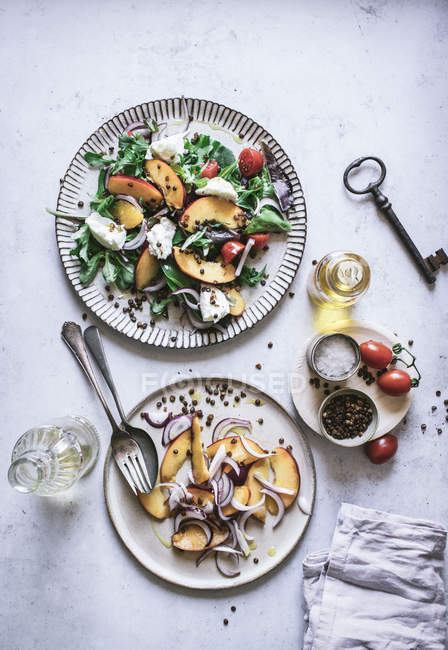 Сверху тарелки с салатами для гурманов из персиков, красный лук, сыр, масло и черный перец на столе — стоковое фото