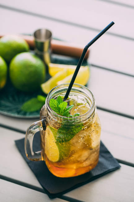 Mojito cocktail prepared with lime, mint, rum, soda and ice in mason jar on table with ingredients — Stock Photo