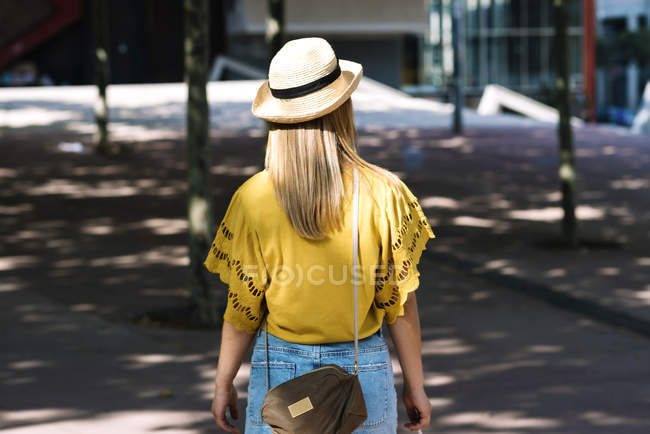Visão traseira da jovem mulher loira elegante em chapéu de palha andando na cidade no dia de verão — Fotografia de Stock