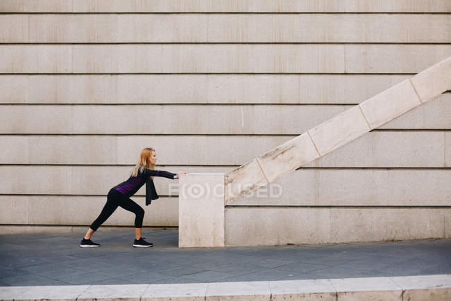 Giovane donna bionda che si estende su una scala dopo una sessione di corsa — Foto stock