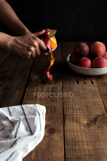 Pêssegos maduros saborosos em prato e mãos descascando pêssego — Fotografia de Stock