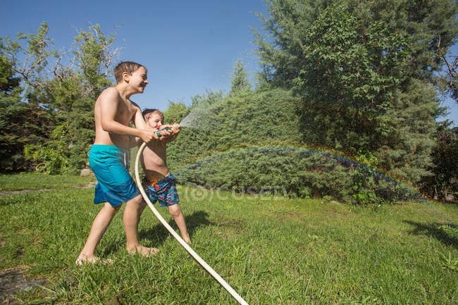 I bambini piccoli in costume da bagno spruzzano acqua tenendo insieme il tubo del giardino — Foto stock