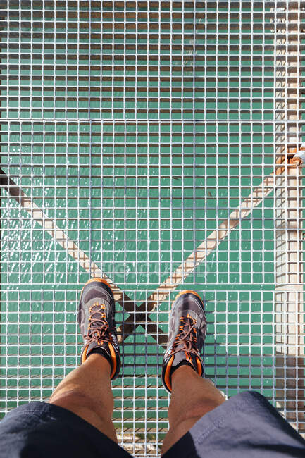 Vista superior da colheita pernas de homem irreconhecíveis em pé na ponte de montanha alta sobre um rio. — Fotografia de Stock