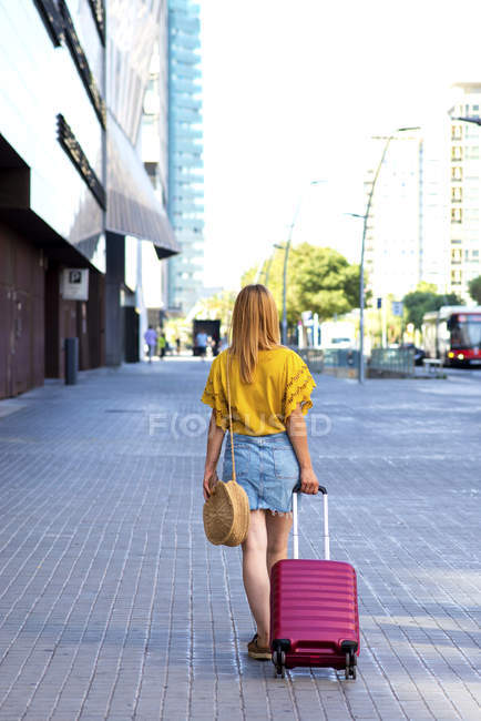 Назад вид молодой туристки с чемоданом, идущей по улице — стоковое фото
